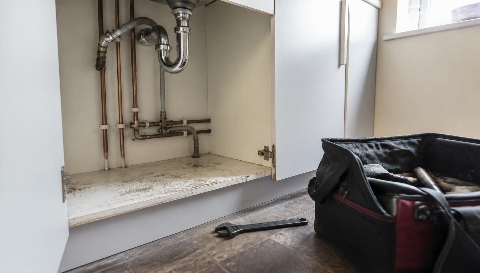 Copper pipework and waste trap under a kitchen sink with plumbing tools